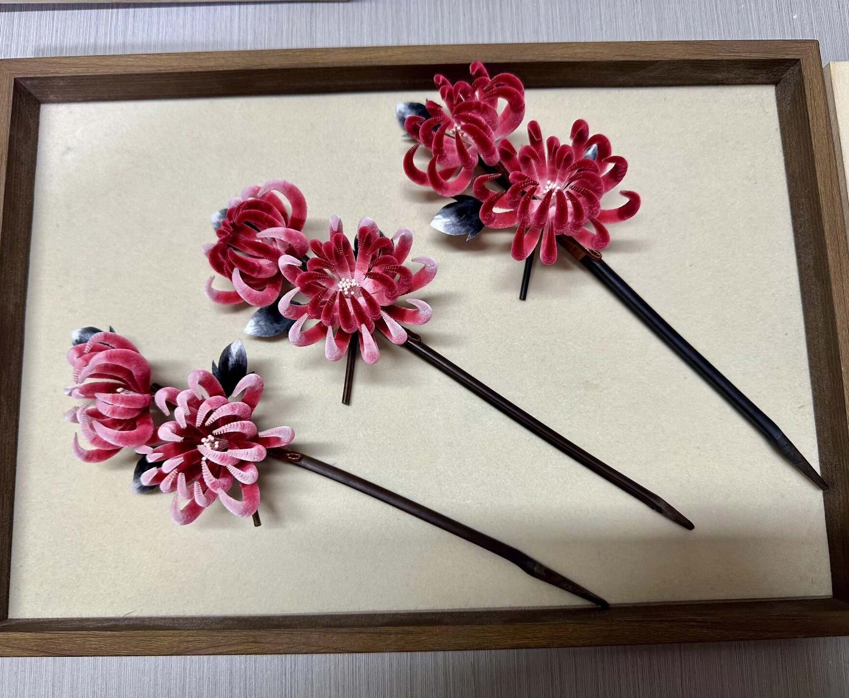Handmade Ronghua double-head red chrysanthemum hair stick set in mulberry silk velvet flower with wooden pins and dark leaves, displayed on wooden tray