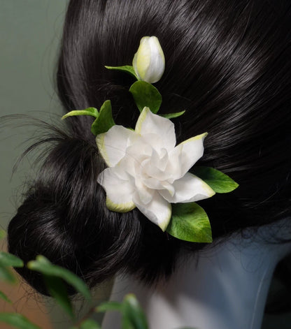 Handmade Ronghua white gardenia hairpin in mulberry silk velvet with green leaves and bud on black hair stick, worn in low bun