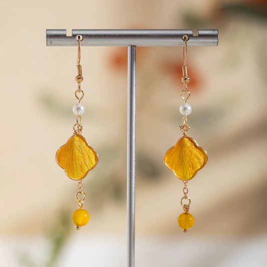 Handmade Ronghua yellow four-leaf clover drop earrings in mulberry silk velvet with gold details on display stand