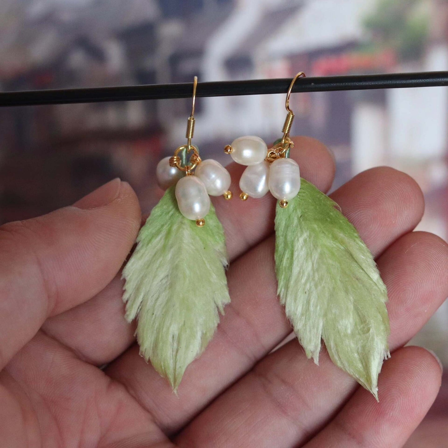Handmade Ronghua green silk velvet leaf drop earrings with freshwater pearls on gold hooks, held in hand