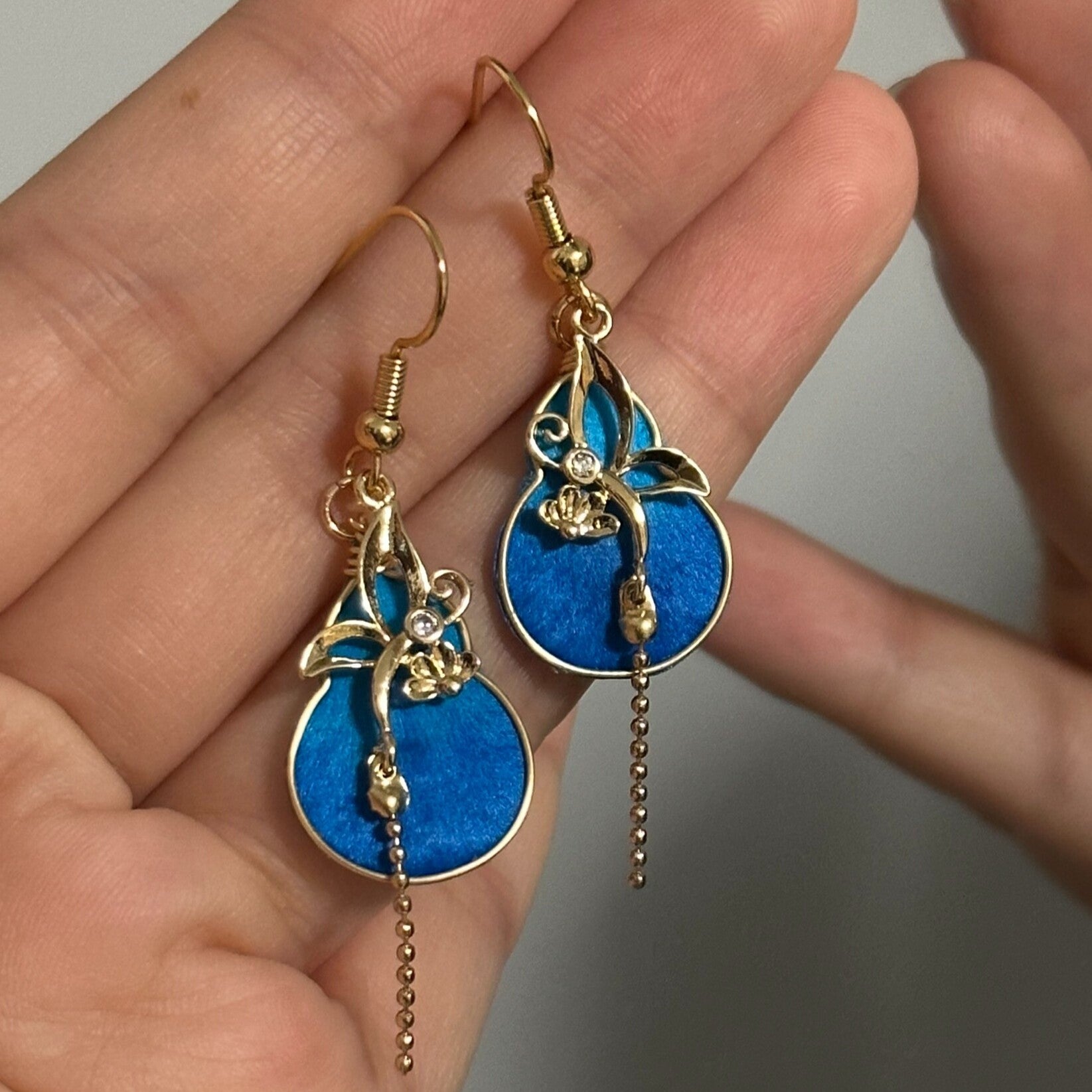 Handmade Ronghua royal blue silk velvet gourd drop earrings with gold vine details and crystal bead tassel, held in hand