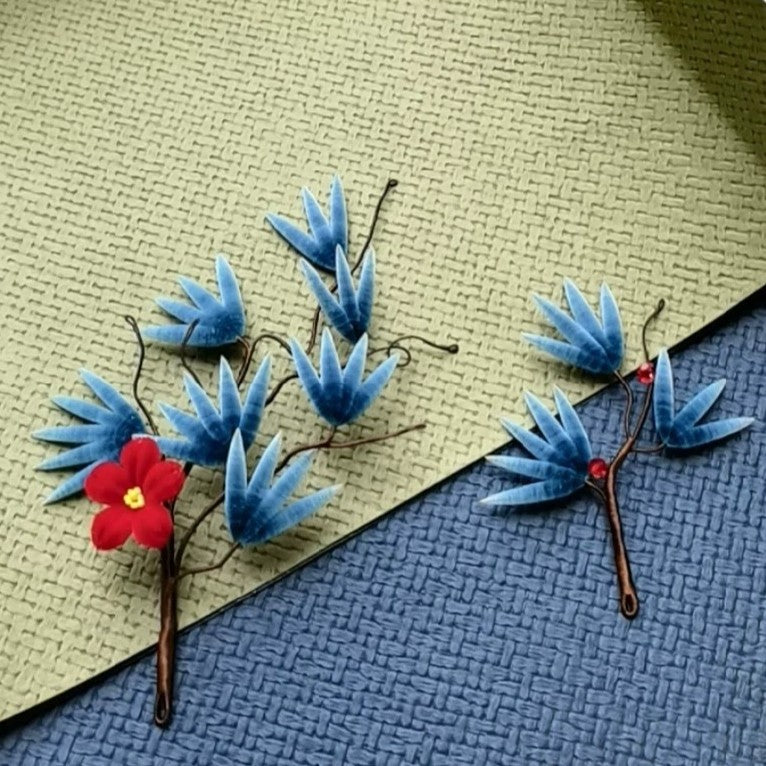 Handmade Ronghua pine needle hair stick in blue-green mulberry silk velvet with red plum blossom accent, displayed on textured background