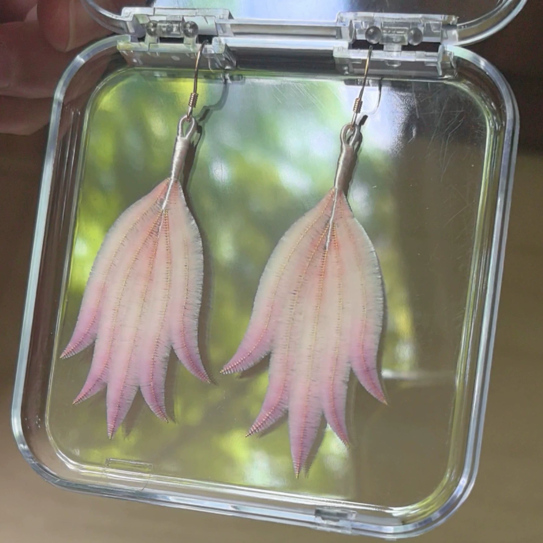 Close-up of soft pink-white gradient Ronghua silk feather earrings showing fine textured petals