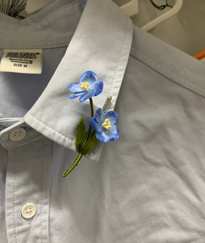 Close-up of sky-blue Ronghua silk star flowers with white edges and green leaf on stick pin