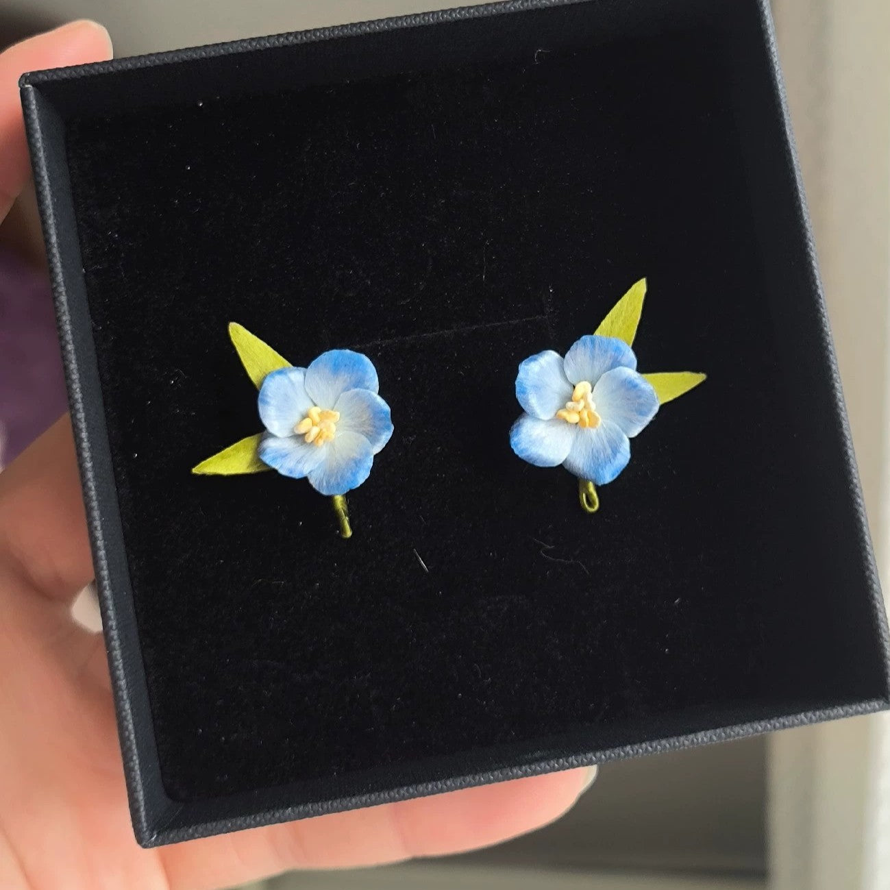 Close-up of miniature Ronghua silk star flowers in sky-blue-white with green leaf and metal post