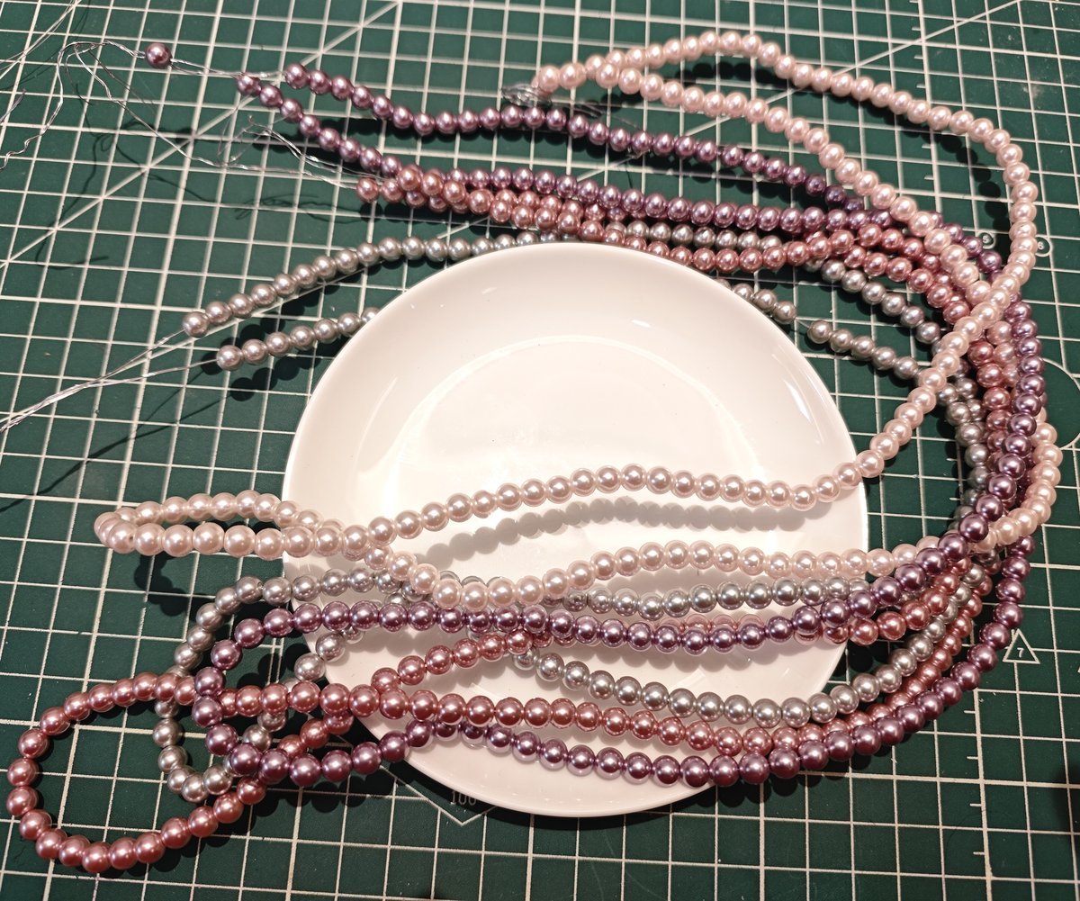 Assorted blush pink, purple, and lavender glass imitation pearl beads in strands on cutting mat, high-quality craft supplies for handmade accessories and sewing projects