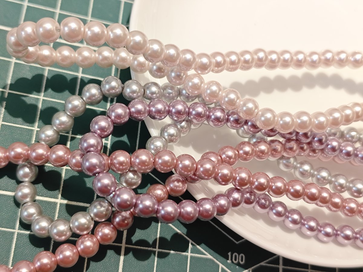 Pastel pink and lavender glass pearl bead strands close-up on crafting mat, premium faux pearls for DIY jewelry and decorations