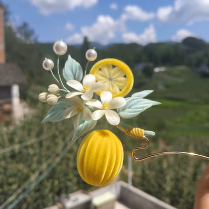 Handmade Ronghua summer lemon hairpin with yellow lemon fruit, white flowers, pearls and green leaves against blue sky background