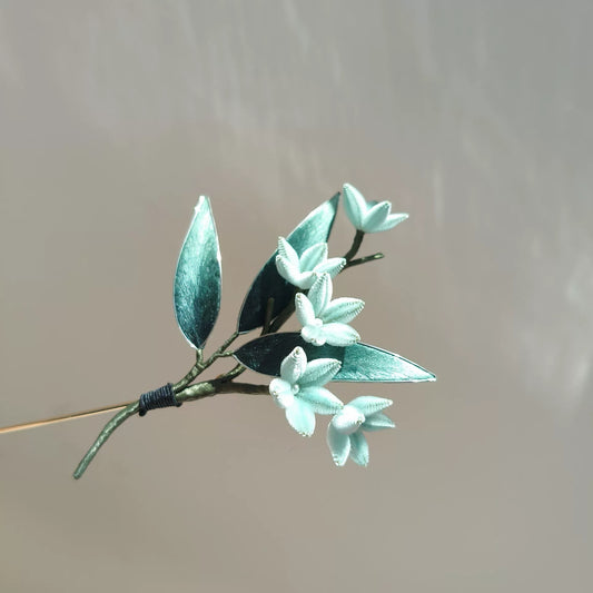 Handmade Ronghua bamboo leaf brooch with white silk velvet flowers and teal green leaves on neutral background