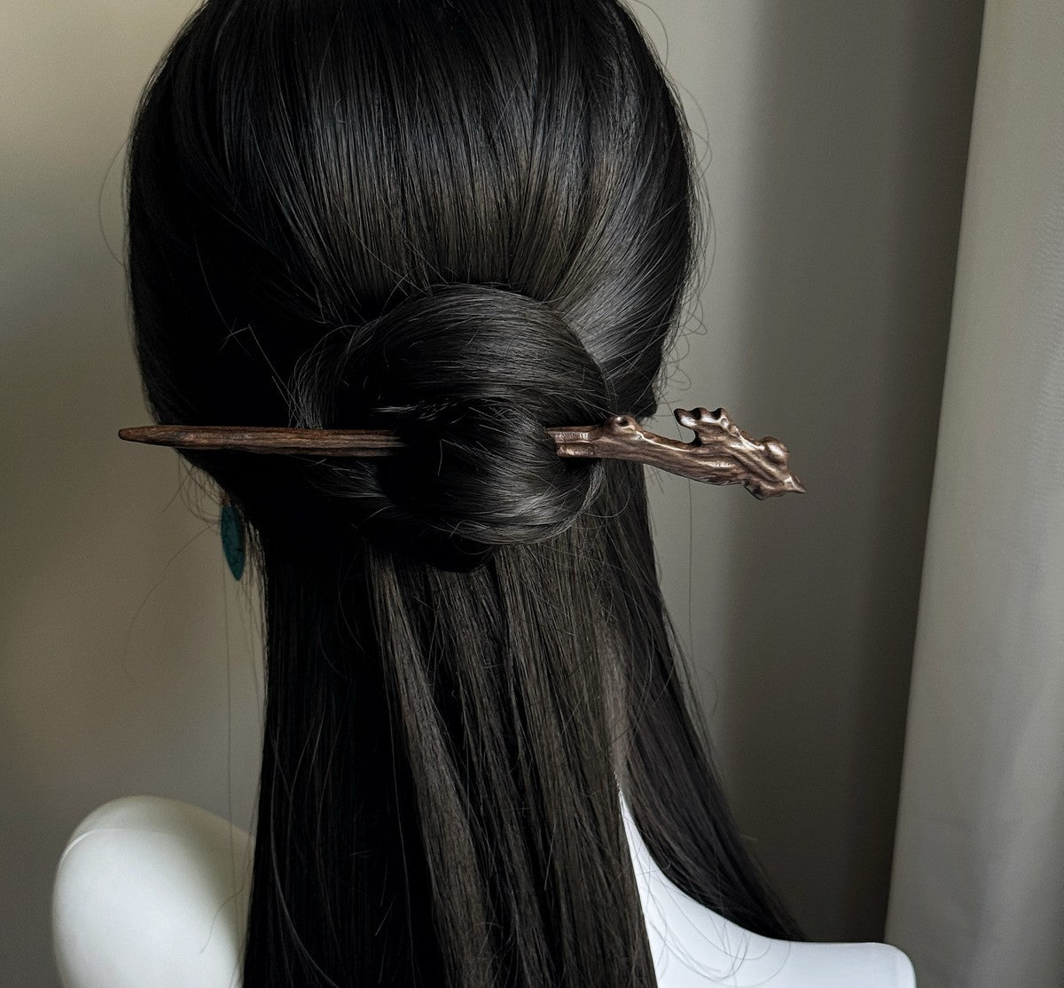 Rear view of long dark hair in a low bun secured with natural rosewood hair stick featuring branch design
