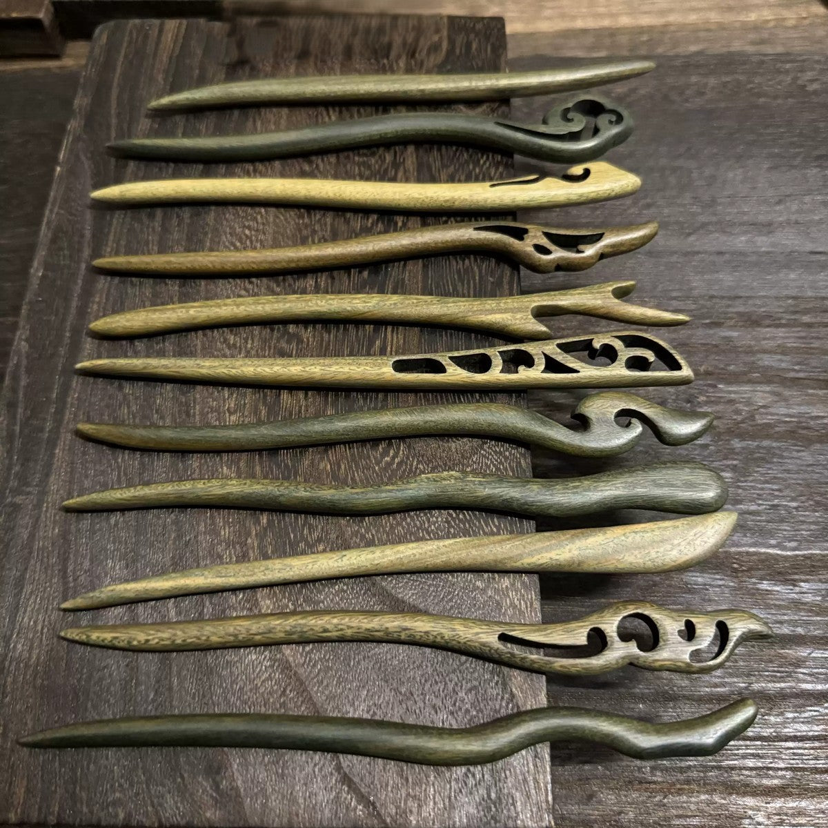 Set of 10+ natural Green Sandalwood hair sticks from premium heartwood with carved designs on wooden background.