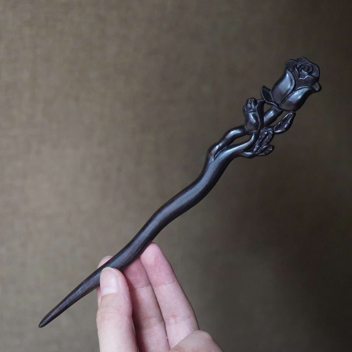 Natural African Blackwood hair stick with detailed rose flower carving on neutral background.