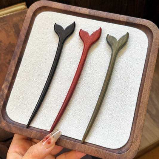 Set of three natural African Blackwood hair sticks with fish tail design in different shades on wooden tray.