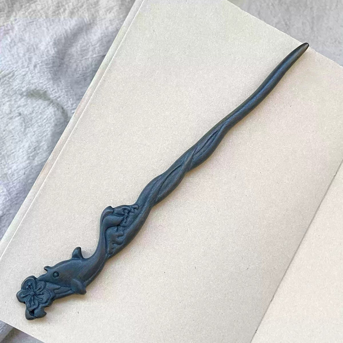 Natural Green Sandalwood hair stick with blue whale carving 20cm on open book background.