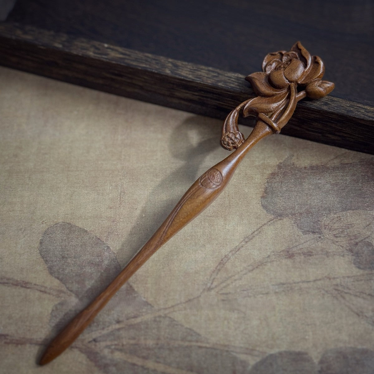Natural Golden Phoebe hair stick with floating lotus carving 19.8cm on textured background.